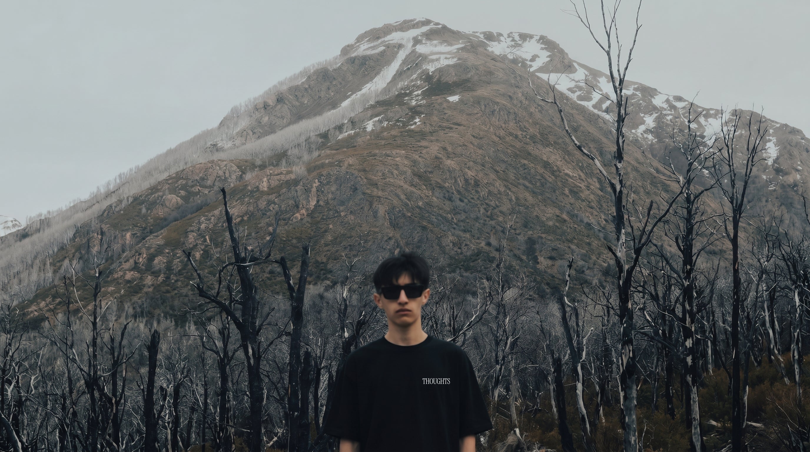 Person wearing sunglasses standing in front of a mountain with snow patches